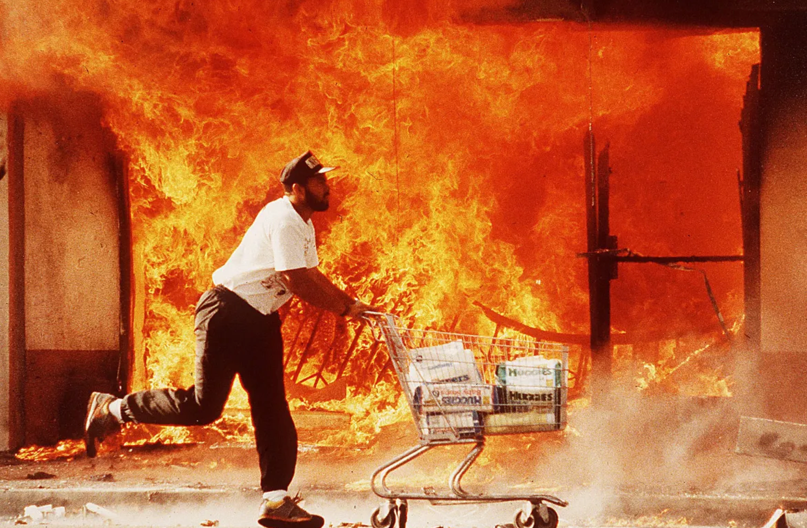 Rodney King Riots - A man wheels a shopping cart full of diapers past a burning market on April 30, 1991.